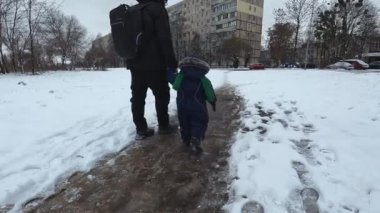 Father and son walk along a snowy path in the city on a winter day. Parent and child are walking. Copy space - winter holidays concept, family vacation, nature, fun