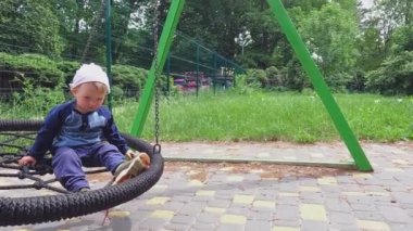 Üzgün küçük bir çocuk parkta sallanarak oturuyor. Kopyalama alanı - aktif eğlence konsepti, yaşam tarzı, şehir yürüyüşleri, rüya, çocuk psikolojisi, eğitim, sıcak sonbahar havası