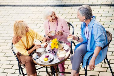 Güzel ve mutlu yetişkin kadınlardan oluşan bir grup açık havada buluşuyorlar ve bar kafeteryasında buluşuyorlar şık, modaya uygun yaşlı insanlarla buluşuyorlar ve bir kafede eğleniyorlar.