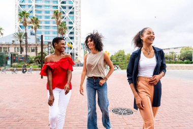 Mutlu güzel İspanyol asıllı Güney Amerikalı ve siyah kadınlar dışarıda buluşup eğleniyorlar siyah yetişkin kadın arkadaşlar birlikte vakit geçiriyorlar ve alışveriş için şehirde dolaşıyorlar.