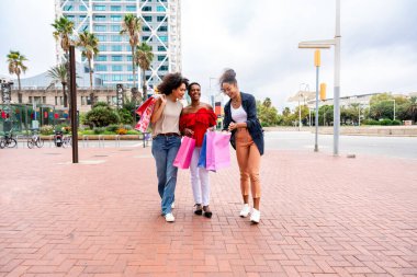 Mutlu güzel İspanyol asıllı Güney Amerikalı ve siyah kadınlar dışarıda buluşup eğleniyorlar siyah yetişkin kadın arkadaşlar birlikte vakit geçiriyorlar ve alışveriş için şehirde dolaşıyorlar.