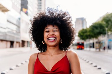 Güzel, genç, mutlu, afro kıvırcık saçlı Afrikalı bir kadın şehirde geziyor.