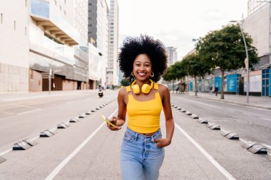 Güzel, genç, mutlu, afro kıvırcık saçlı Afrikalı bir kadın şehirde geziyor.