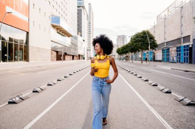 Güzel, genç, mutlu, afro kıvırcık saçlı Afrikalı bir kadın şehirde geziyor.
