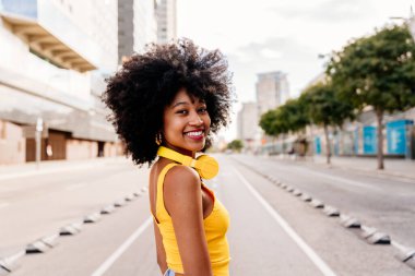 Güzel, genç, mutlu, afro kıvırcık saçlı Afrikalı bir kadın şehirde geziyor.