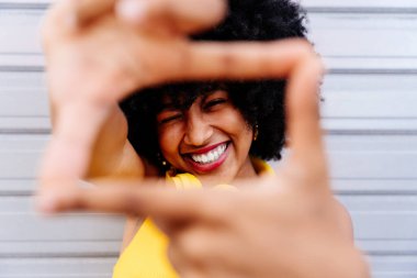 Güzel, genç, mutlu, afro kıvırcık saçlı Afrikalı bir kadın, renkli duvar arkasında neşeli siyah öğrenci portresi.