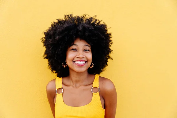 Beautiful young happy african woman with afro curly hairstyle strolling in the city - Cheerful black student portrait on colorful wall background