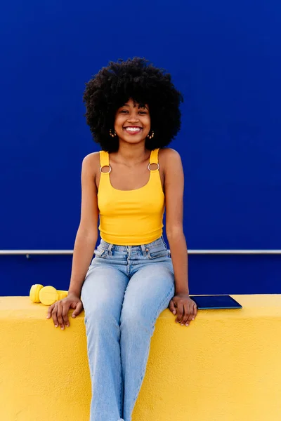 Beautiful young happy african woman with afro curly hairstyle strolling in the city - Cheerful black student portrait on colorful wall background