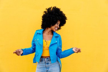 Güzel, genç, mutlu, afro kıvırcık saçlı Afrikalı bir kadın, renkli duvar arkasında neşeli siyah öğrenci portresi.