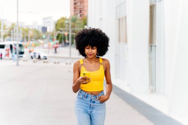 Güzel, genç, mutlu, afro kıvırcık saçlı Afrikalı bir kadın şehirde geziyor.