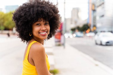 Güzel, genç, mutlu, afro kıvırcık saçlı Afrikalı bir kadın şehirde geziyor.