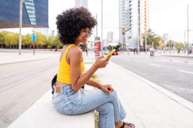 Güzel, genç, mutlu, afro kıvırcık saçlı Afrikalı bir kadın şehirde geziyor.