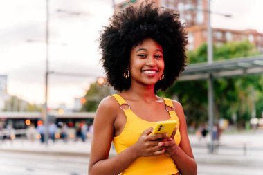 Güzel, genç, mutlu, afro kıvırcık saçlı Afrikalı bir kadın şehirde geziyor.