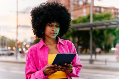 Güzel, genç, mutlu, afro kıvırcık saçlı Afrikalı bir kadın şehirde geziniyor.