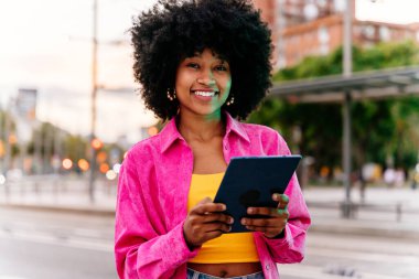 Güzel, genç, mutlu, afro kıvırcık saçlı Afrikalı bir kadın şehirde geziniyor.