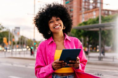 Güzel, genç, mutlu, afro kıvırcık saçlı Afrikalı bir kadın şehirde geziniyor.