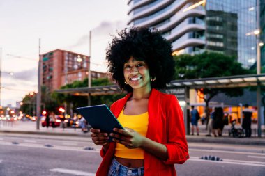Güzel, genç, mutlu, afro kıvırcık saçlı Afrikalı bir kadın şehirde geziniyor.