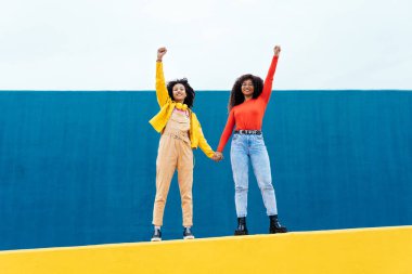 Genç mutlu kadınlar mavi ve sarı renkli duvarlarda poz veriyorlar. Genç kızlar okuldan sonra birlikte vakit geçiriyorlar.