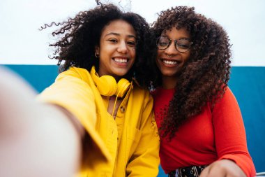 Genç mutlu kadınlar akıllı telefonlarıyla selfie çekiyorlar. Gençler okuldan sonra dışarıda eğleniyorlar.