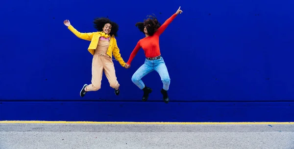 年轻快乐的女人在户外跳舞和玩乐 在一个黄色和蓝色的现代城市地区 青少年们正在用智能手机和耳机听音乐 — 图库照片