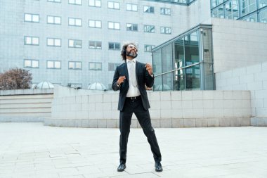 Genç girişimci iş adamı ofis dışında müzik dinleyip dans ediyor. İş hayatında özgürlük ve başarı kavramı