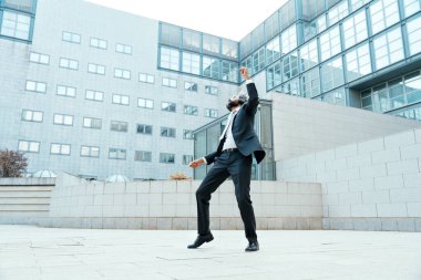 Genç girişimci iş adamı ofis dışında müzik dinleyip dans ediyor. İş hayatında özgürlük ve başarı kavramı