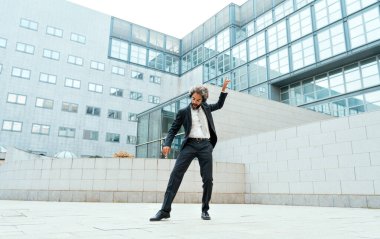 Genç girişimci iş adamı ofis dışında müzik dinleyip dans ediyor. İş hayatında özgürlük ve başarı kavramı