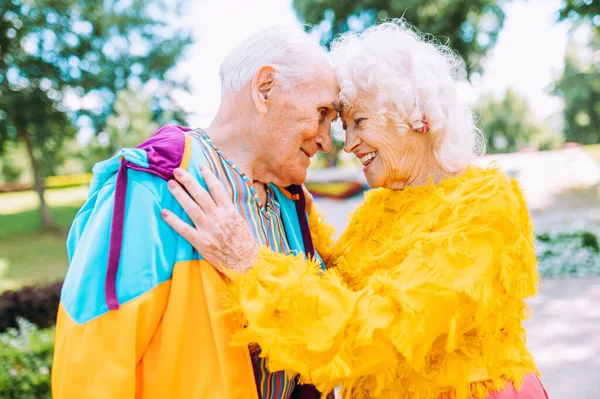 Old modern couple dressing fashionable colored clothes. Youthful grandmother and grandfather having fun outdoor and going wild. Representation of elderly people feeling young inside