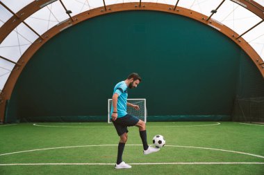 Futbol serbest stil oyuncusunun suni çim kortunda top oynarken çekilmiş sinematik bir görüntüsü. Spor ve insan yaşam tarzı kavramı