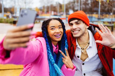 Çok ırklı genç aşıklar kışın açık havada buluşuyorlar sosyal medya uygulamasını akıllı telefonlarda kullanıyorlar, kışlık ceketler giyiyorlar ve eğleniyorlar - Kentsel alanda çok ırklı binyıllar birleşiyor, gençlik ve sosyal özgürlükler kavramları