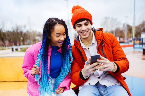 冬にはスマートフォンのソーシャルメディアアプリを使用して屋外でデート愛好家の多人種の若いカップル 冬のジャケットを着て 楽しみを持って 都市部での多民族ミレニアルボンディング 若者や社会的関係についての概念 — ストック写真