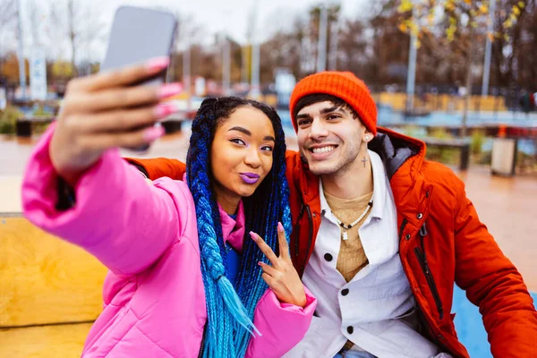 Multiracial young couple of lovers dating outdoors in winter using social media app on smartphone, wearing winter jackets and having fun - Multiethnic millennials bonding in a urban area, concepts about youth and social releationships