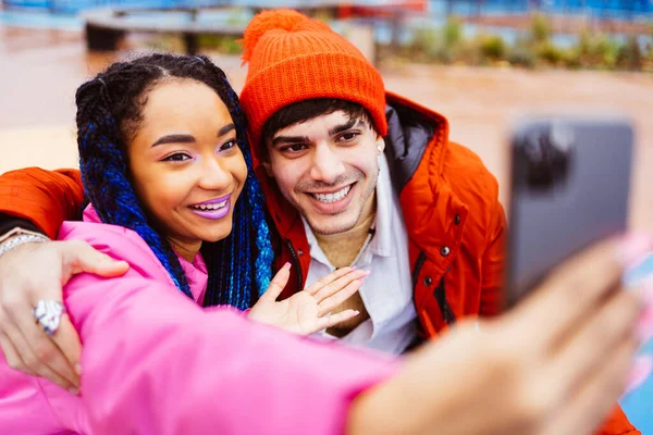 冬にはスマートフォンのソーシャルメディアアプリを使用して屋外でデート愛好家の多人種の若いカップル 冬のジャケットを着て 楽しみを持って 都市部での多民族ミレニアルボンディング 若者や社会的関係についての概念 — ストック写真