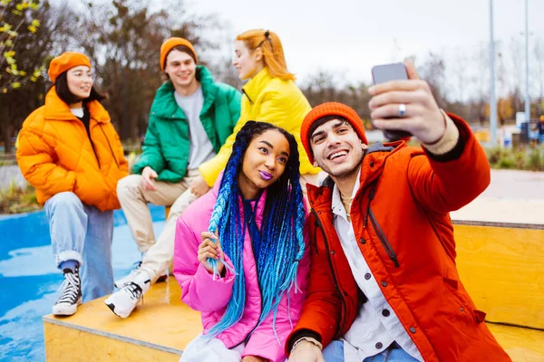 冬に屋外で会う若い幸せな友人の多人種グループ 冬のジャケットを着て 楽しみを持っています カップルは ソーシャルメディアのためのスマートフォンで自撮り 都市部での多民族ミレニアルボンディング 若者と社会的関係についての概念 — ストック写真