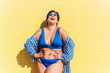 Beautiful and confident plus size woman having fun at the beach, posing on colorful wall background -  concepts about body acceptance, body positive, self confidence and body care