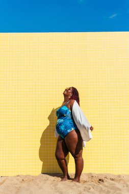 Beautiful and confident plus size woman having fun at the beach, posing on colorful wall background -  concepts about body acceptance, body positive, self confidence and body care