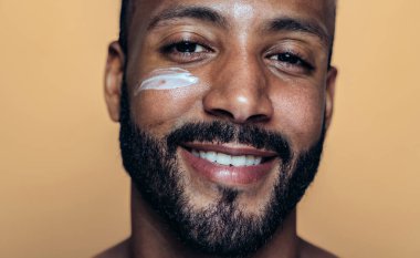 Tenine bakan genç bir adamın görüntüsü. Güzellik stüdyosu cilt bakımı ve kişisel hijyen ürünleri hakkında çekim yapıyor..