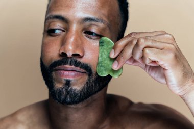 Tenine bakan genç bir adamın görüntüsü. Güzellik stüdyosu cilt bakımı ve kişisel hijyen ürünleri hakkında çekim yapıyor..