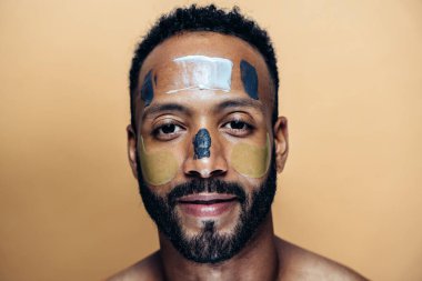 Tenine bakan genç bir adamın görüntüsü. Güzellik stüdyosu cilt bakımı ve kişisel hijyen ürünleri hakkında çekim yapıyor..