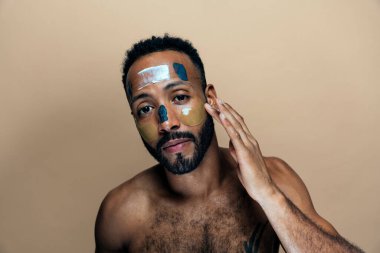 Tenine bakan genç bir adamın görüntüsü. Güzellik stüdyosu cilt bakımı ve kişisel hijyen ürünleri hakkında çekim yapıyor..