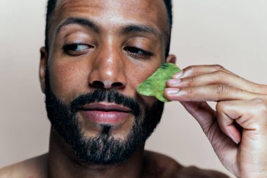 Tenine bakan genç bir adamın görüntüsü. Güzellik stüdyosu cilt bakımı ve kişisel hijyen ürünleri hakkında çekim yapıyor..