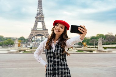 Beautiful young woman visiting paris and the eiffel tower. Parisian girl with red hat and fashionable clothes having fun in the city center and landmarks area