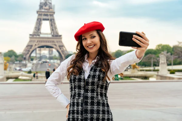 Beautiful young woman visiting paris and the eiffel tower. Parisian girl with red hat and fashionable clothes having fun in the city center and landmarks area