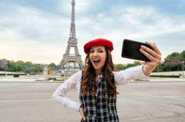 Beautiful young woman visiting paris and the eiffel tower. Parisian girl with red hat and fashionable clothes having fun in the city center and landmarks area