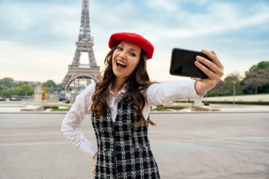 Beautiful young woman visiting paris and the eiffel tower. Parisian girl with red hat and fashionable clothes having fun in the city center and landmarks area
