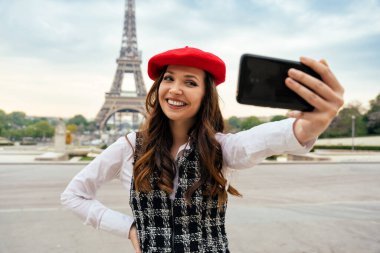 Beautiful young woman visiting paris and the eiffel tower. Parisian girl with red hat and fashionable clothes having fun in the city center and landmarks area