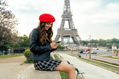 Beautiful young woman visiting paris and the eiffel tower. Parisian girl with red hat and fashionable clothes having fun in the city center and landmarks area