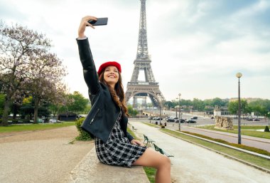 Beautiful young woman visiting paris and the eiffel tower. Parisian girl with red hat and fashionable clothes having fun in the city center and landmarks area