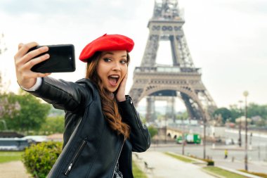Beautiful young woman visiting paris and the eiffel tower. Parisian girl with red hat and fashionable clothes having fun in the city center and landmarks area
