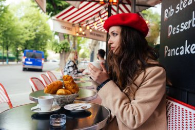 Beautiful young woman visiting paris and the eiffel tower. Parisian girl with red hat and fashionable clothes having fun in the city center and landmarks area